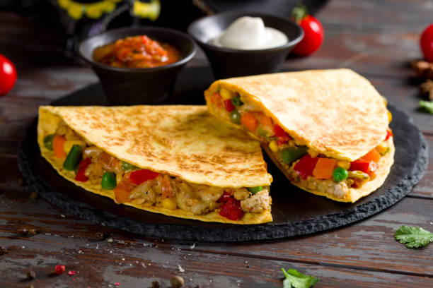 istock Mexican Quesadilla with chicken, vegetables, cheese and sauces on black stone plate 1412538015