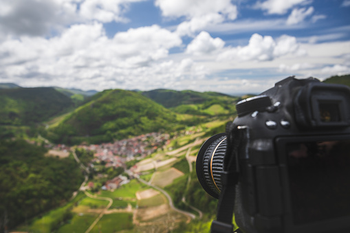 Close-up of a unrecognizable reflex camera, focus on foreground with copy space, while photographing Cerdon small village of Bugey, Alps mountains near Jura massif, in Ain, Auvergne-Rhone-Alpes region in France.
