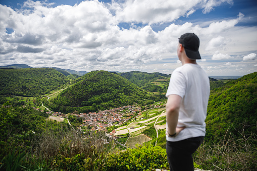 Rear view of one young man, hiker in summer enjoying the view on small wine village of Cerdon in Bugey mountains, Alps near Jura massif, in Ain, Auvergne-Rhone-Alpes region in France.