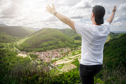 Rear view of one young man, hiker in summer enjoying the view on small wine village of Cerdon in Bugey mountains, Alps near Jura massif, in Ain, Auvergne-Rhone-Alpes region in France.