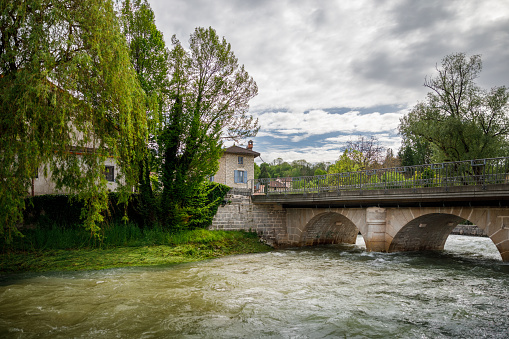 View of an old stone bridge, with Le Veyron river crossing the village of Poncin. This image was taken during a sunny summer day in Bugey, Alps mountains near Jura massif, in Ain, Auvergne-Rhone-Alpes region in France.