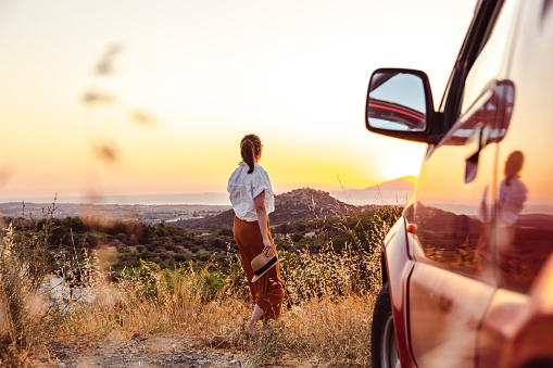 Rear view of a young woman taking a break from driving a car and enjoying the sunset
