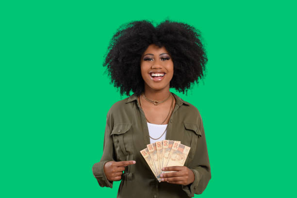 mulher segurando dinheiro, jovem mulher sorridente segurando dinheiro brasileiro, fundo verde - real people - fotografias e filmes do acervo