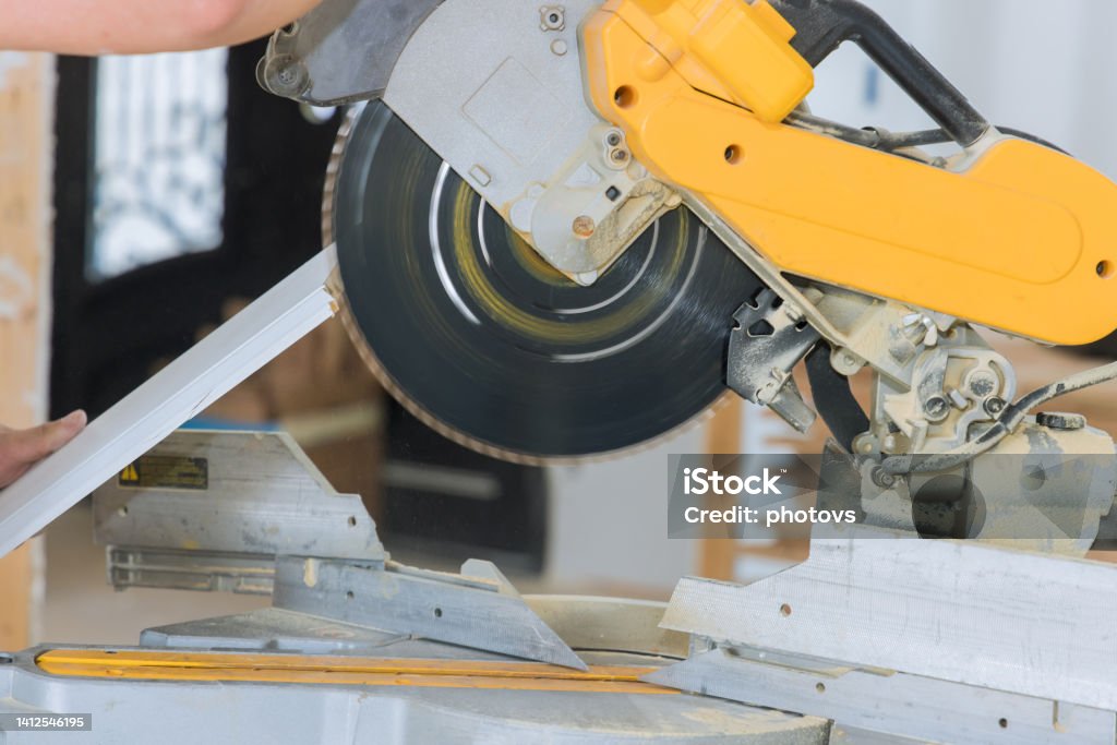 Construction workers are cutting wood moldings baseboards on the circular saw for the finishing work on the construction projects Construction workers are cutting wood moldings baseboards on circular saw for the finishing work the construction projects Construction Site Stock Photo