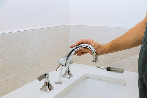 A plumber at work assembles and installs a water faucet in the bathroom