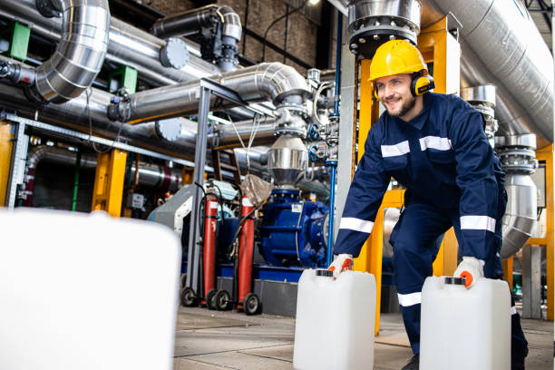 Petrochemical industrial worker carrying plastic canisters with chemicals inside refinery production plant. stock photo