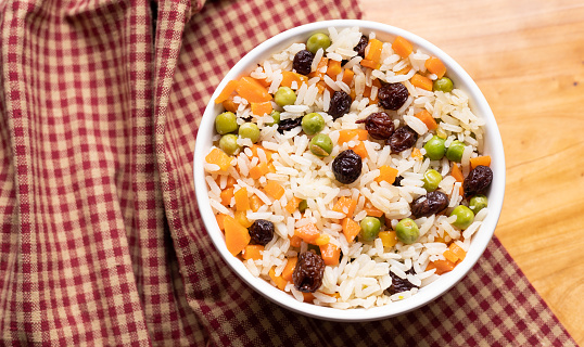 Greek-Style Rice ( Arroz à grega ) in white bowl. Brazilian food. In this image contains rice, raisins, carrots and peas.