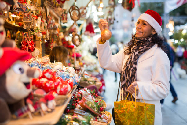 Positive woman selecting gifts at christmas fair Happy latin woman standing at counter and choosing christmas decorations. New year's fair. christmas market stock pictures, royalty-free photos & images