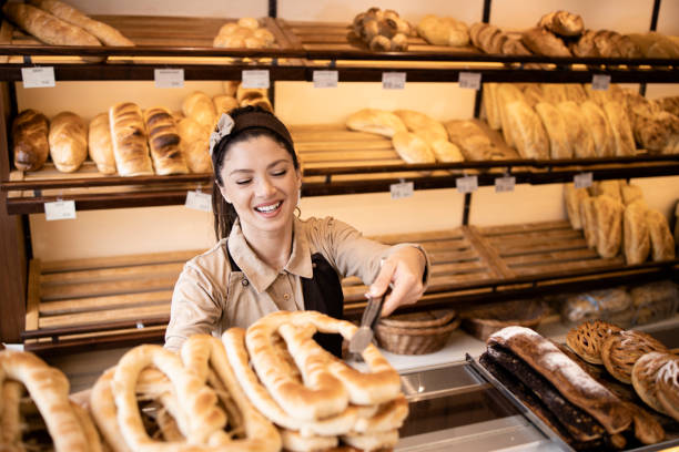 Beautiful smiling bakery worker selling fresh pastry to the customer in bakery shop. stock photo