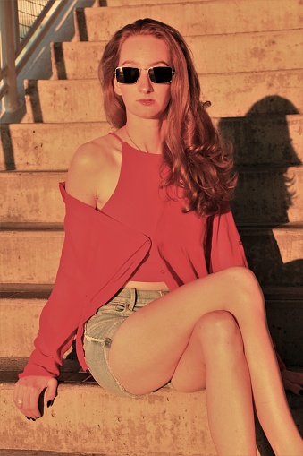 A model from Paraguay showing her sunglasses. She is wearing a red shirt and cover with denim shorts.