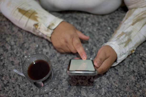 Portrait of a Latin woman in the kitchen, using her cellphone, and having some coffee on the table.