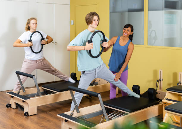 l’instructeur de pilates aide l’adolescent à faire des exercices avec un anneau - pilates machine photos et images de collection