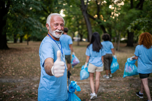 Senior man and group of volunteers cleaning nature together