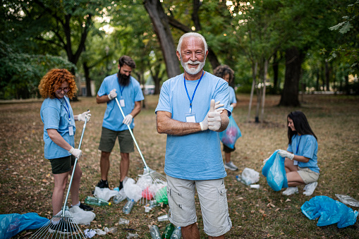 Senior man and group of volunteers cleaning nature together