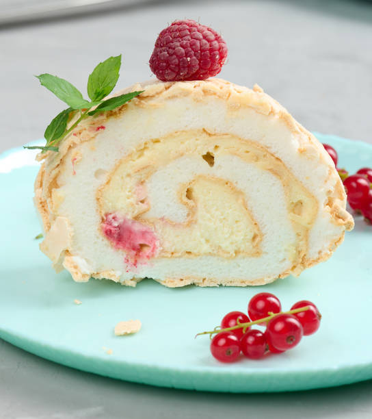 istock Baked meringue roll with red berries on a round plate, white background 1412556680