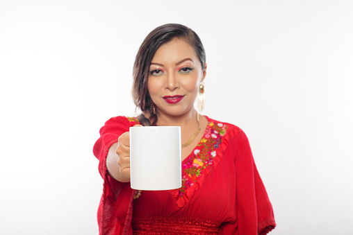 Mexican woman holding white cup, focus on cup. Re-portrait of woman holding cup with arm extended in front. Focus on the cup.