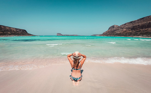 Caucasian woman in blue bikini enjoying her vacations in Greece, walking on a beautiful sandy beach.
