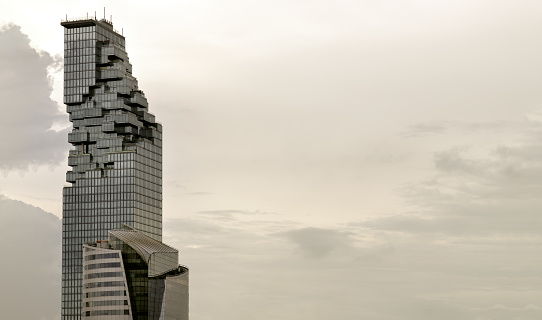 Bangkok, Thailand - 08 Jul 2022 : Architectural view of Angular geometric mirror cladding on a modern building with repeating structure and sky and clouds at sunset. Space for text, No focus, specifically.