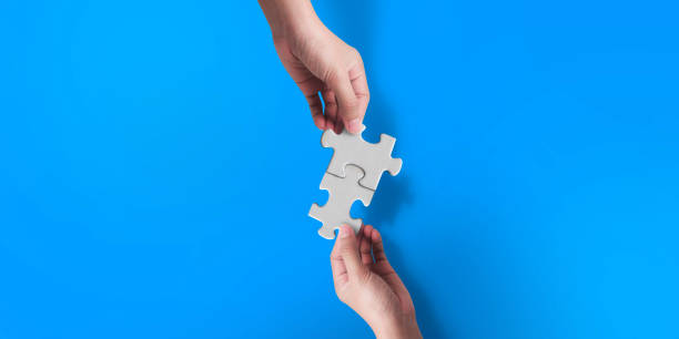 istock Two hand joining two matching puzzle pieces on blue background, conceptual image of teamwork. 1412565847