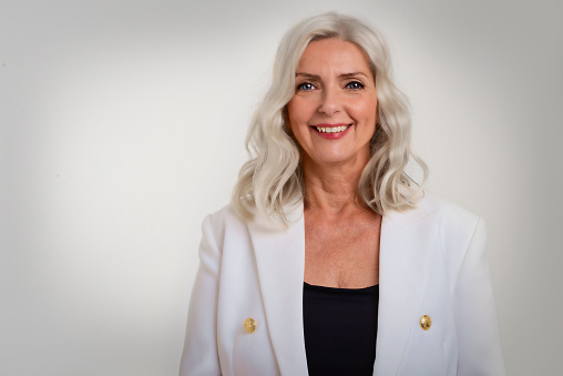 Portrait of attractive grey haired woman wearing blazer while standing at isolated white background. Copy space.