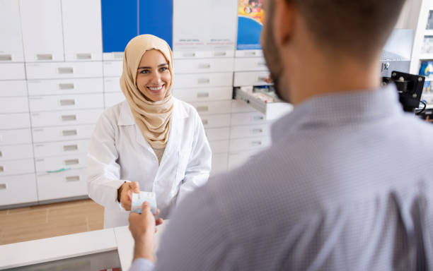 un pharmacien musulman vend des médicaments à un client à la pharmacie - vêtement religieux photos et images de collection