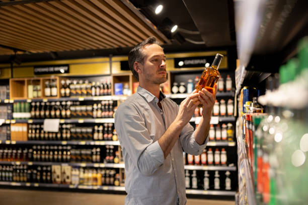 uomo al supermercato che compra una bottiglia di whisky - liquor store foto e immagini stock