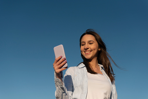 Image with a young woman using a phone and enjoying the outdoors