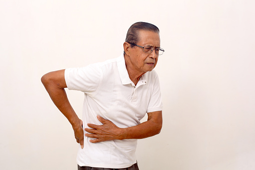 Elderly asian man suffering from low back pain. Isolated on white background with copyspace