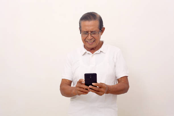 istock Happy elderly asian man standing while holding his cell phone. Isolated on white background 1412573529