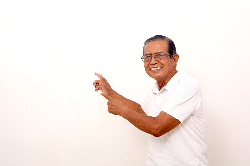 Excited asian old man standing while pointing sideways. Isolated on white background with copyspace