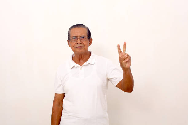 istock Elderly asian man standing while showing two fingers. Isolated on white background. 1412574421