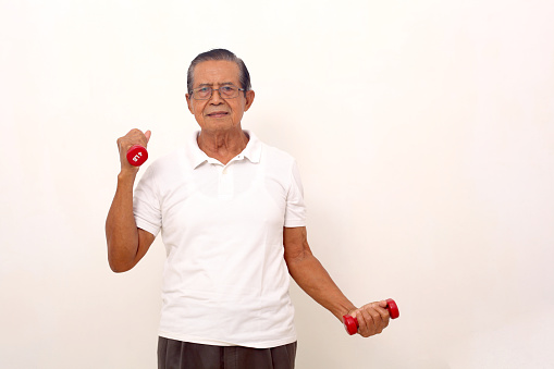 Elderly asian man standing while lifting dumbbells. Isolated on white background with copyspace