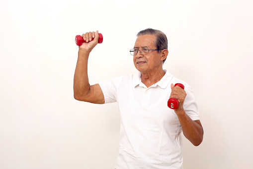 Elderly asian man standing while lifting dumbbells. Isolated on white background.