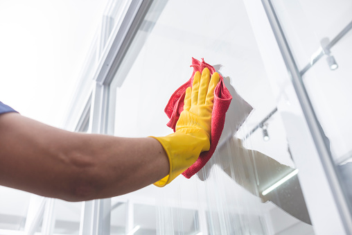 A man wearing yellow gloves wipes clean the surface of a glass window with a red microfiber cloth.
