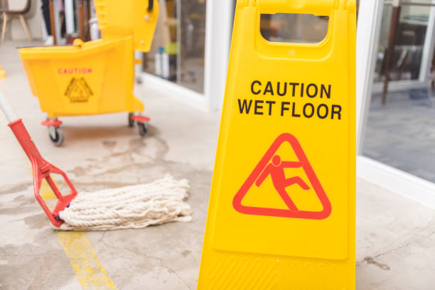 A Caution Wet Floor sign placed to warn passersby while wiping a wet concrete floor with a string mop.