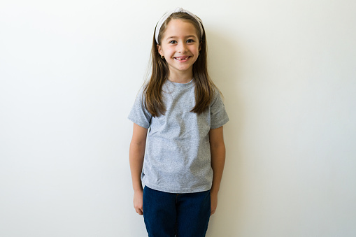 Beautiful little girl with a big smile with a grey mockup t-shirt for design standing in front of a white studio background
