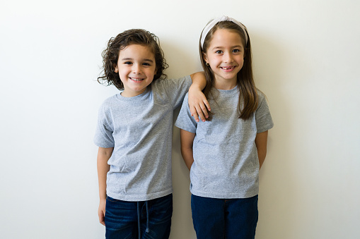 Happy caucasian children showing the front design print of their grey mockup t-shirt against a white background