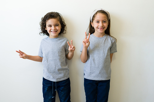 Happy little kids having fun and making the peace sign while wearing grey mockup t-shirts for design print or logo