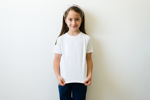 Beautiful little girl showing the design print or logo of her mockup white t-shirt against a background with copy space