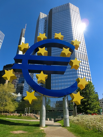 Frankfurt, Germany - April 20, 2022: Euro sign sculpture in a park among modern office towers in Frankfurt and Ukrainian flag- Ukraine and Europe concept