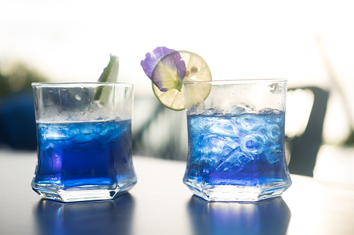 Two glass cups of butterfly pea iced tea. Summer refreshing drink in sunset lighting