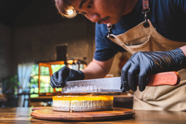 istock Hands of young chef baker cutting slice of mango cheesecake 1412594423
