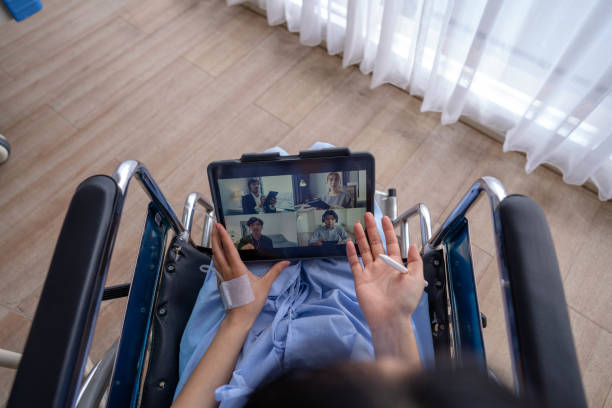 Disabled woman uses laptop to work at hospital. Young disabled woman in wheelchair with a laptop makes video conferencing remotely with partner during his recovery in the hospital. lifehack stock pictures, royalty-free photos & images