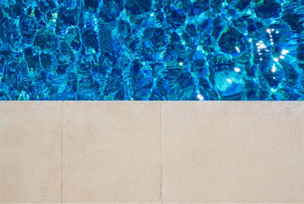 Pool side, top view. Water in the pool with a side. Sun glare in the pool. Selective focus