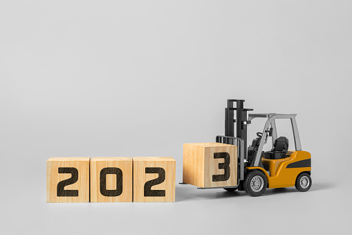 2023 happy new year background. new year industrial concept, forklift carrying box to complete 2023 text isolated on grey background.