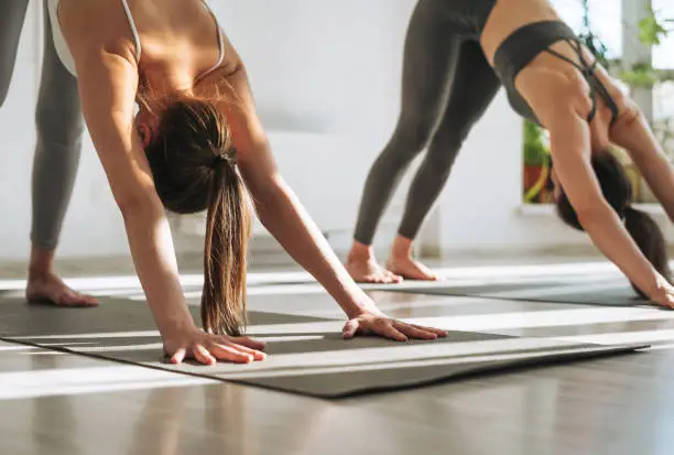 Young fit women practice yoga doing asana in bright yoga studio. Yoga ticher doing sun salutation with student in yoga class