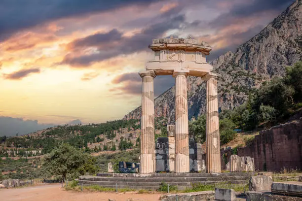 Delphi Greece, Archaeological Site. Ancient Greek temple stone and columns ruins, cloudy sky at sunset background
