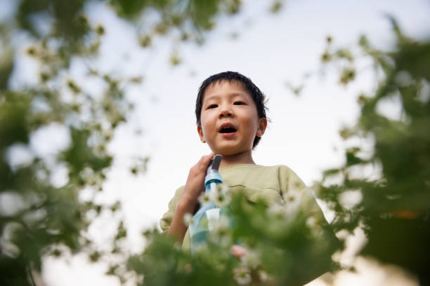 An Asian boy, about 4 years old, wearing a green T-shirt, watered the flowers in front of the flower bed