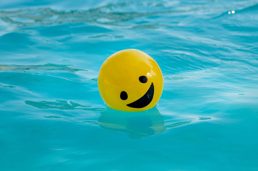 Yellow ball with a smiling face floating on the swimming pool