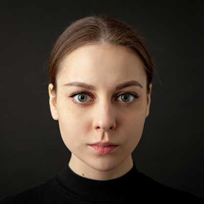 Close up studio portrait of an attractive 20 year old woman with brown hair in a black longsleeve on a black background